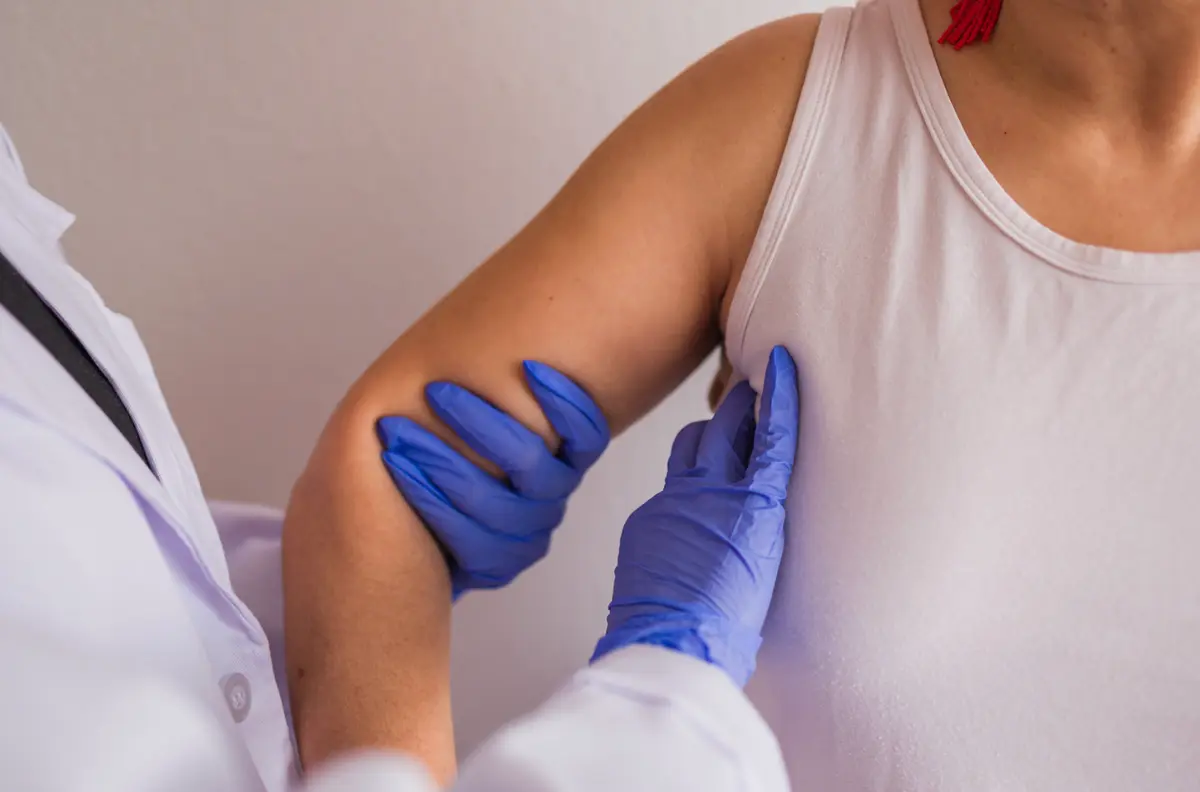 A gloved clinician examining a patient's arm during a health screening